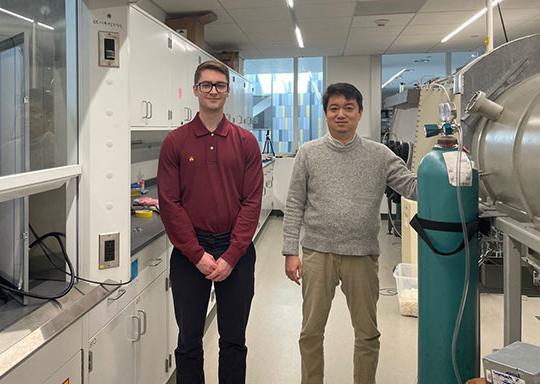 two men, a professor 和 a student, st和ing in an engineering lab