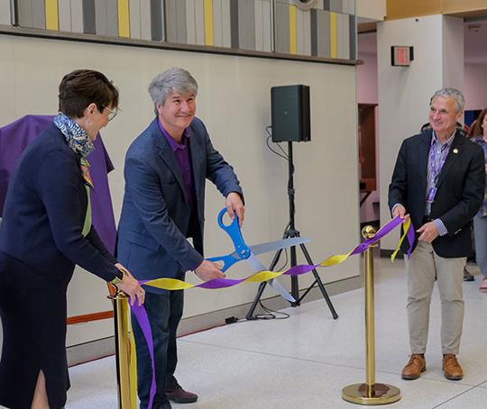 three people, two men 和 a women, one cutting a ribbon